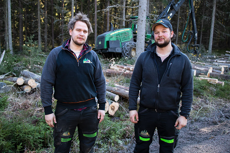 August Luomala Kihlberg och Ollliver Wernestad står ute i skogen framför en grön skogsmaskin